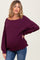 woman wearing a dark purple ribbed maternity sweater and showing her baby bump, paired with blue jeans