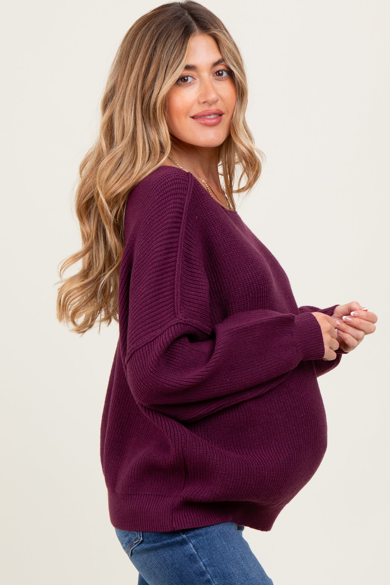 woman wearing a deep purple oversized maternity sweater with a visible baby bump and styled wavy hair