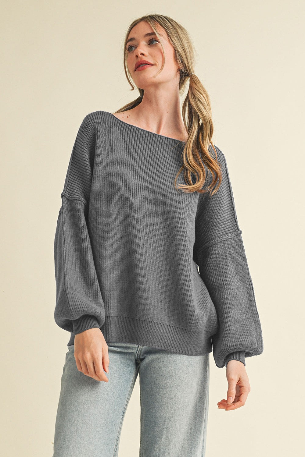 woman wearing a gray ribbed oversized sweater with balloon sleeves and off-the-shoulder neckline, paired with light blue jeans