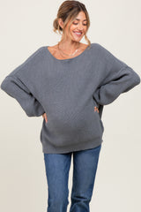 woman wearing a gray oversized ribbed maternity sweater with a visible baby bump and smiling while posing