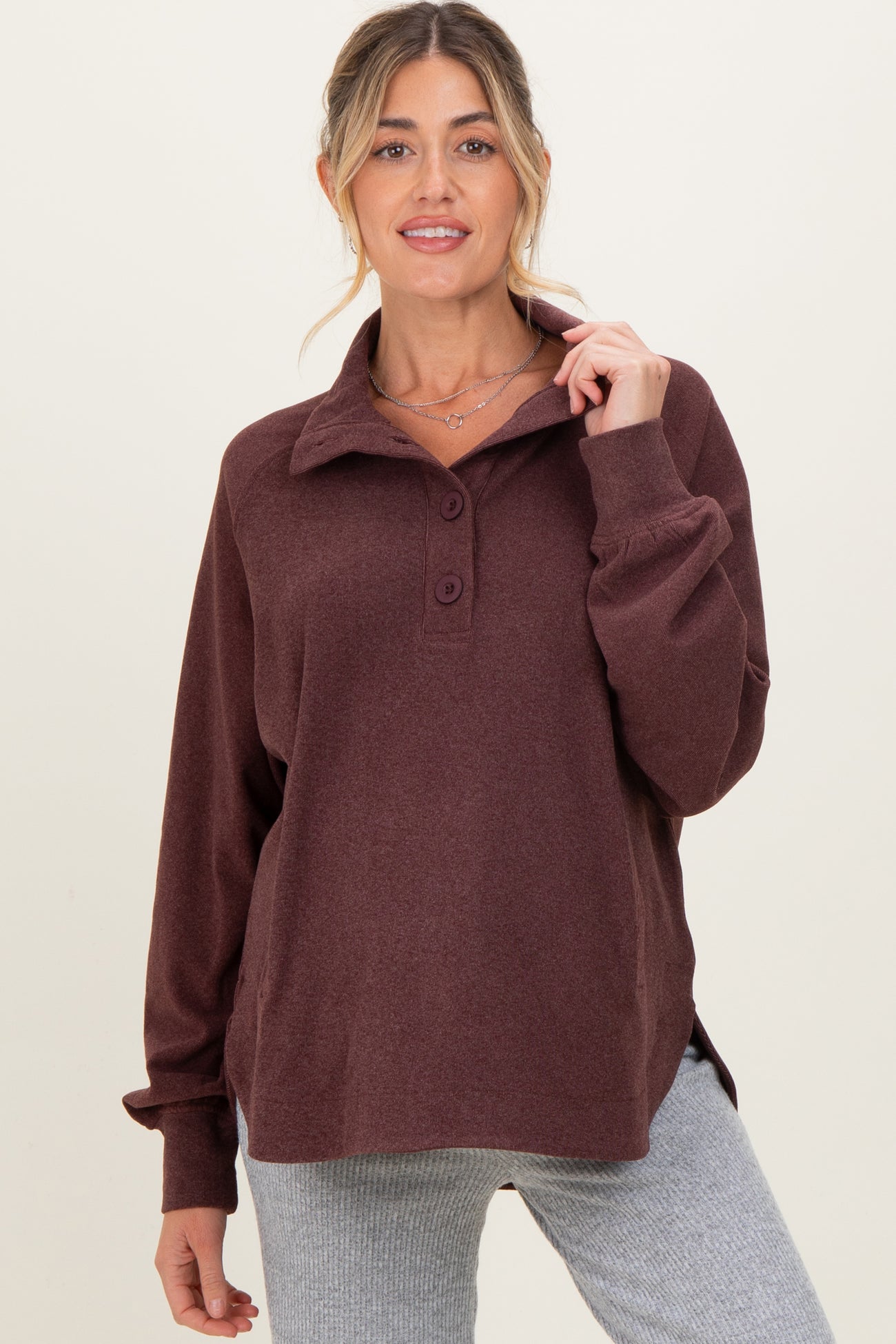woman wearing a burgundy maternity pullover with a collar and button details, paired with gray leggings