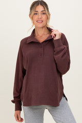 woman wearing a burgundy maternity pullover with a collar and button details, paired with gray leggings