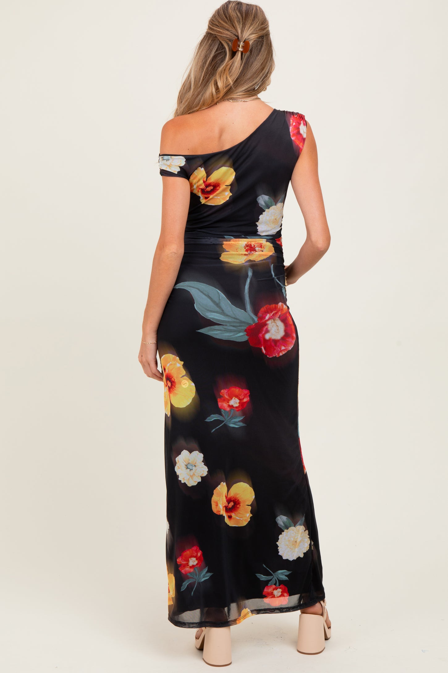 woman wearing a black floral one-shoulder maternity dress, showing a fitted silhouette and ankle-length design