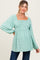 woman wearing a mint green maternity top with square neckline and smocked bodice, showcasing her baby bump