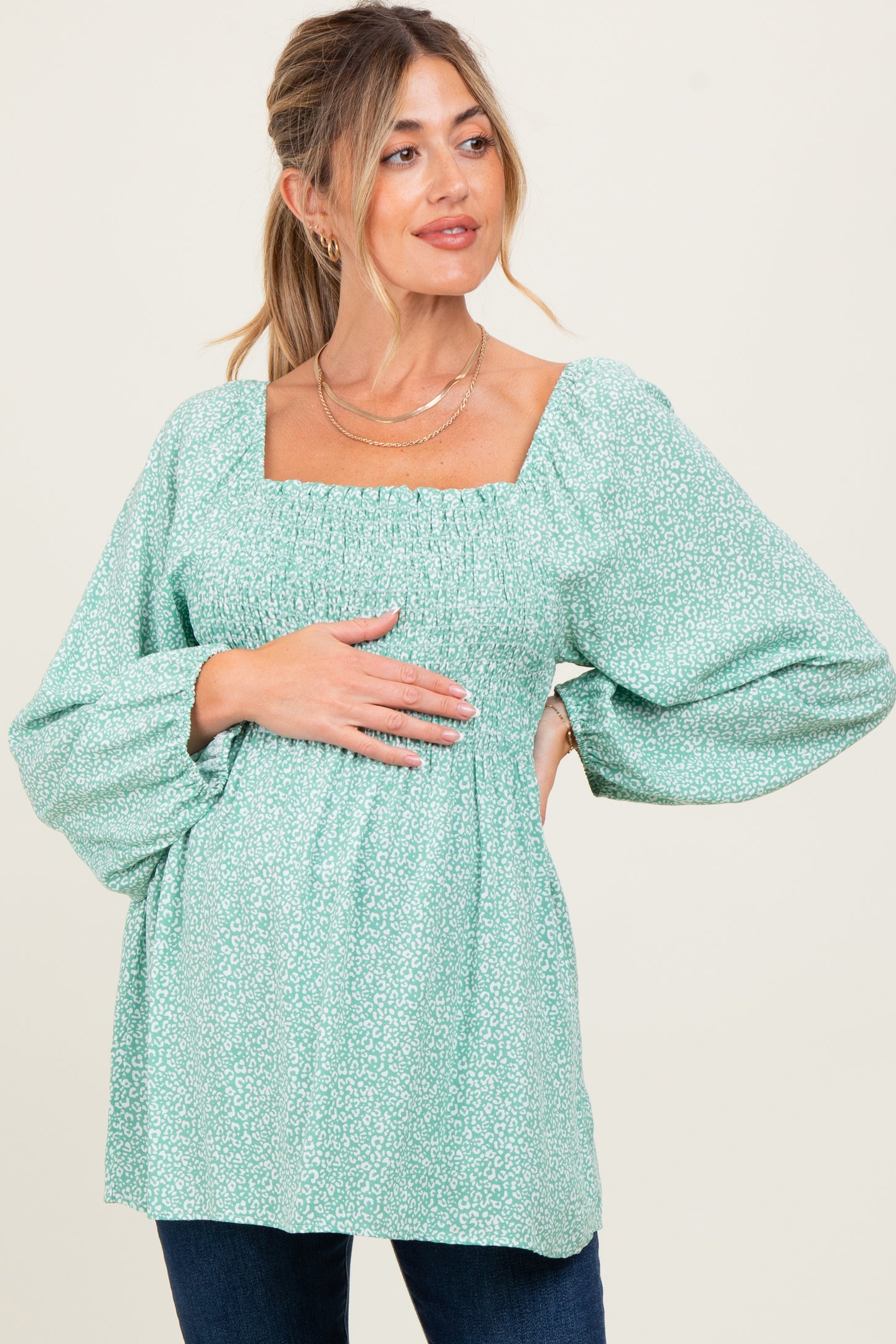 woman wearing a green floral maternity top with square neckline and puffed sleeves, gently resting her hands on her baby bump