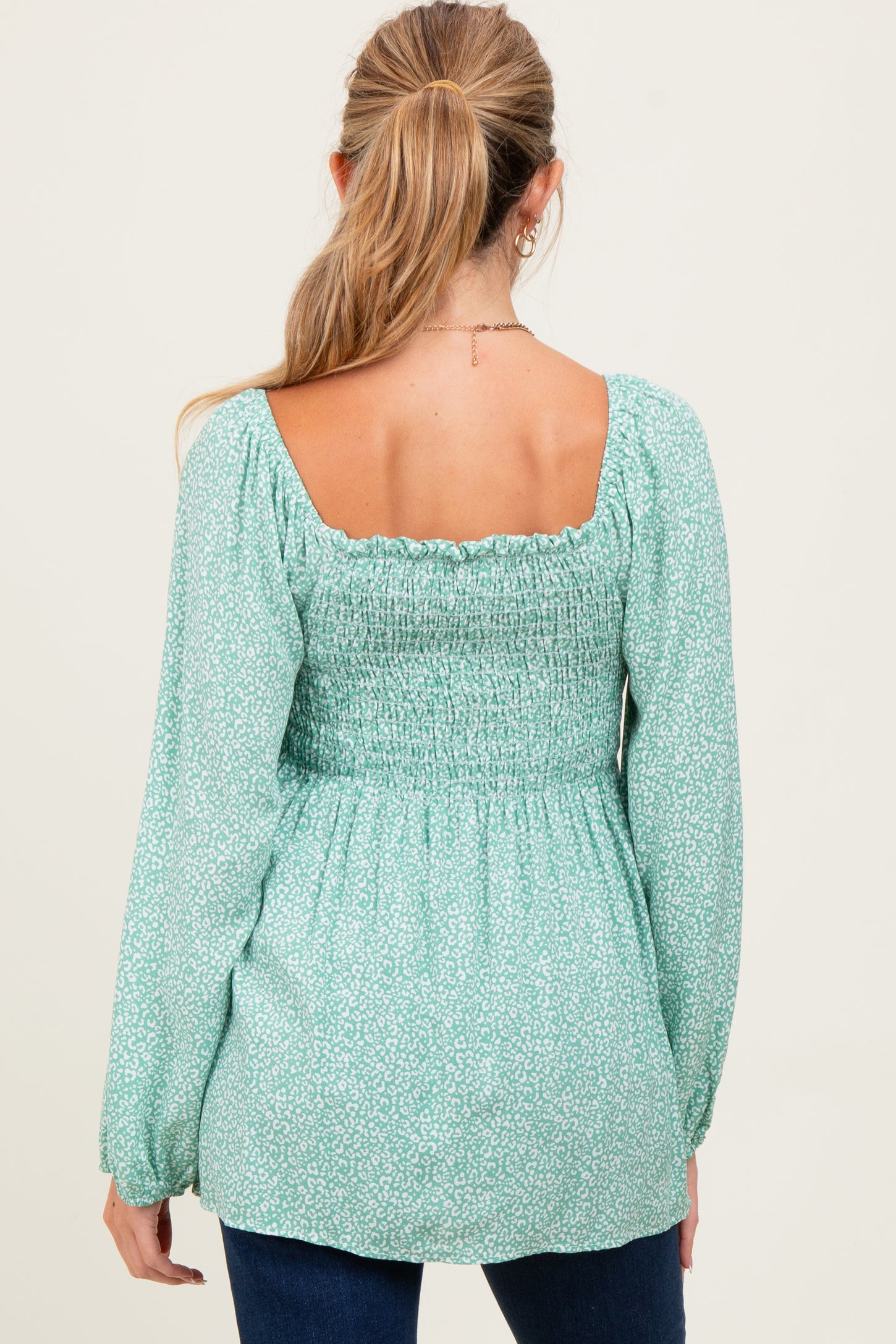 woman wearing a mint green maternity top with a smocked back and long sleeves, view from the back