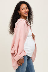 woman wearing a light pink oversized hoodie and blue jeans, showcasing her baby bump