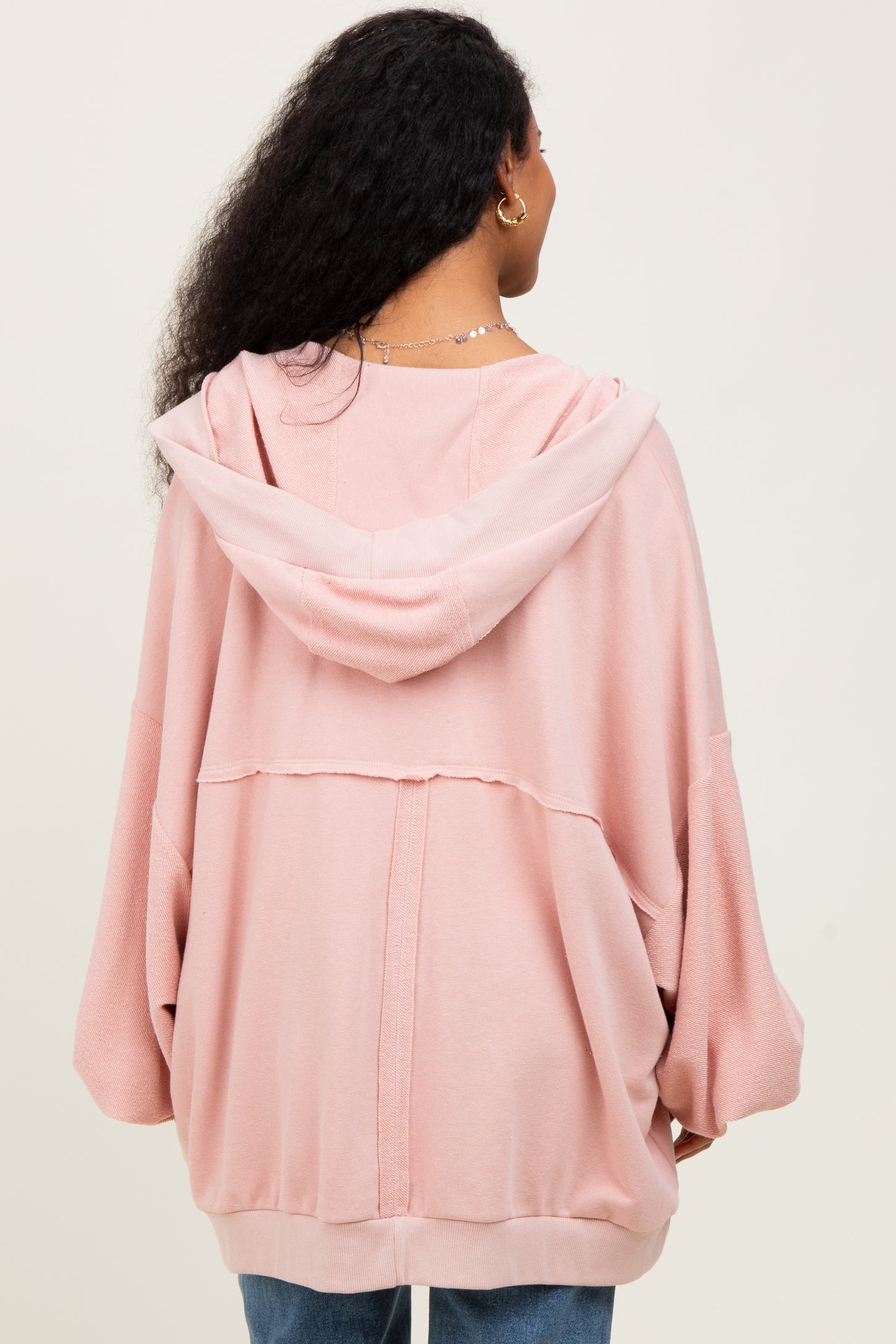 woman wearing a light pink oversized maternity hoodie with a hood and drop sleeves, viewed from the back
