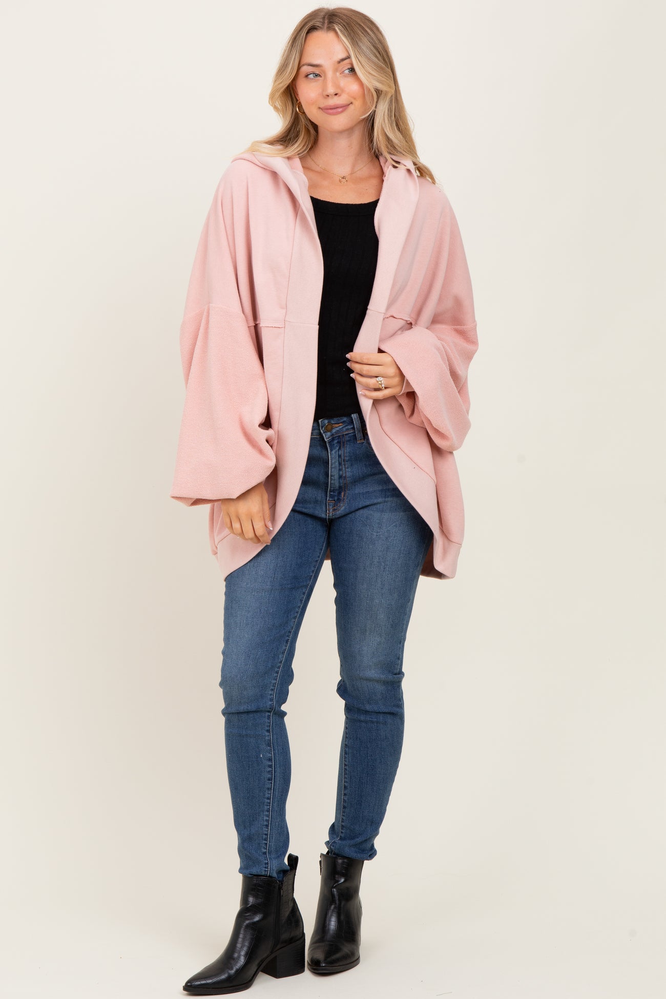 woman wearing a light pink oversized hoodie with bell sleeves, paired with black top and blue skinny jeans