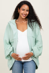 woman wearing a light green maternity zip-up hoodie over a white top and holding her baby bump