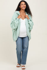 woman wearing a mint green maternity hoodie, white top, and blue jeans, smiling with a visible baby bump