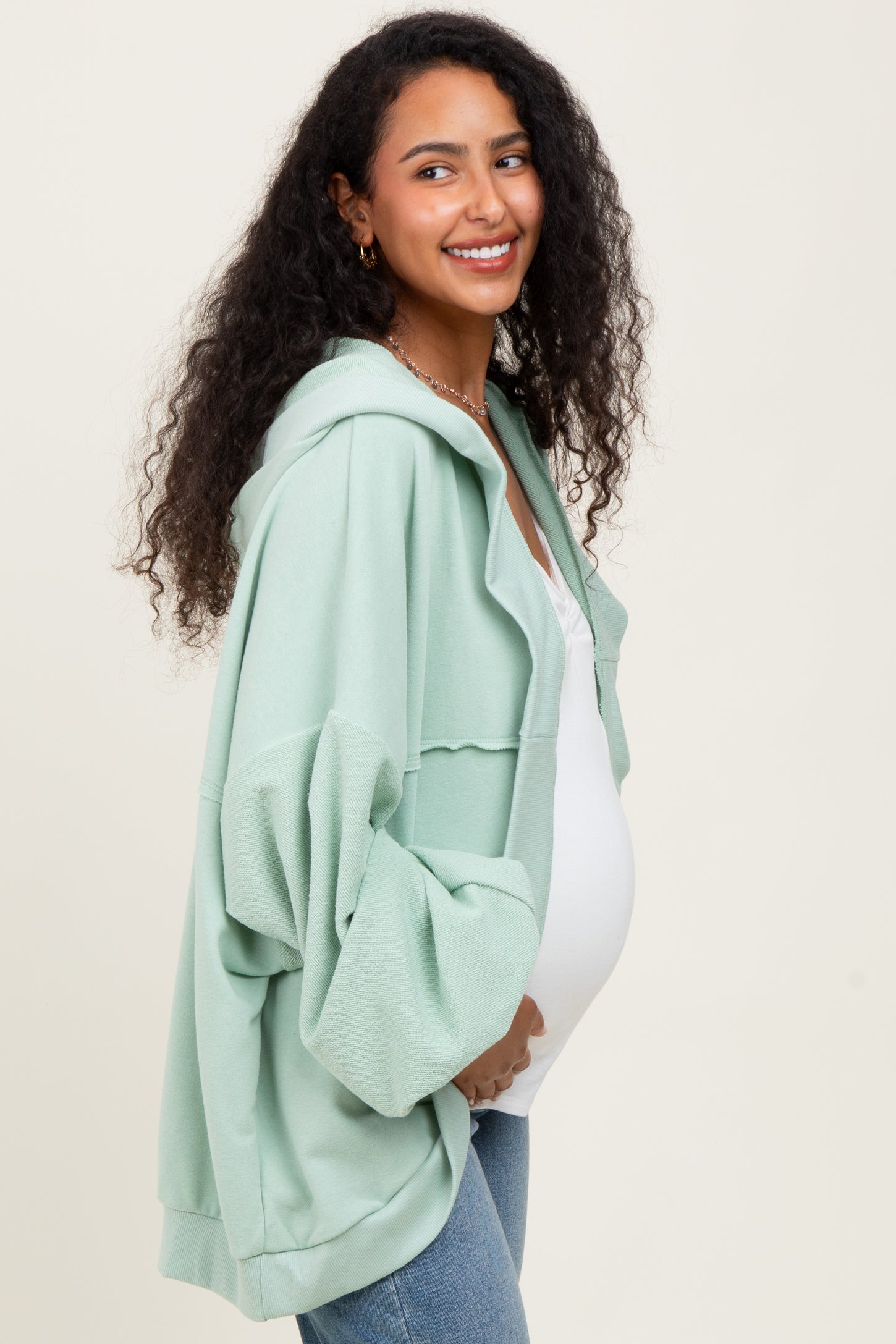 woman wearing a green oversized maternity hoodie and showing her baby bump
