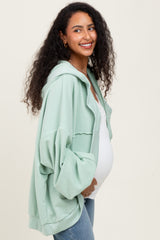 woman wearing a green oversized maternity hoodie and showing her baby bump