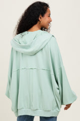 woman wearing a light green oversized maternity hoodie with a hood and relaxed fit, showing her back