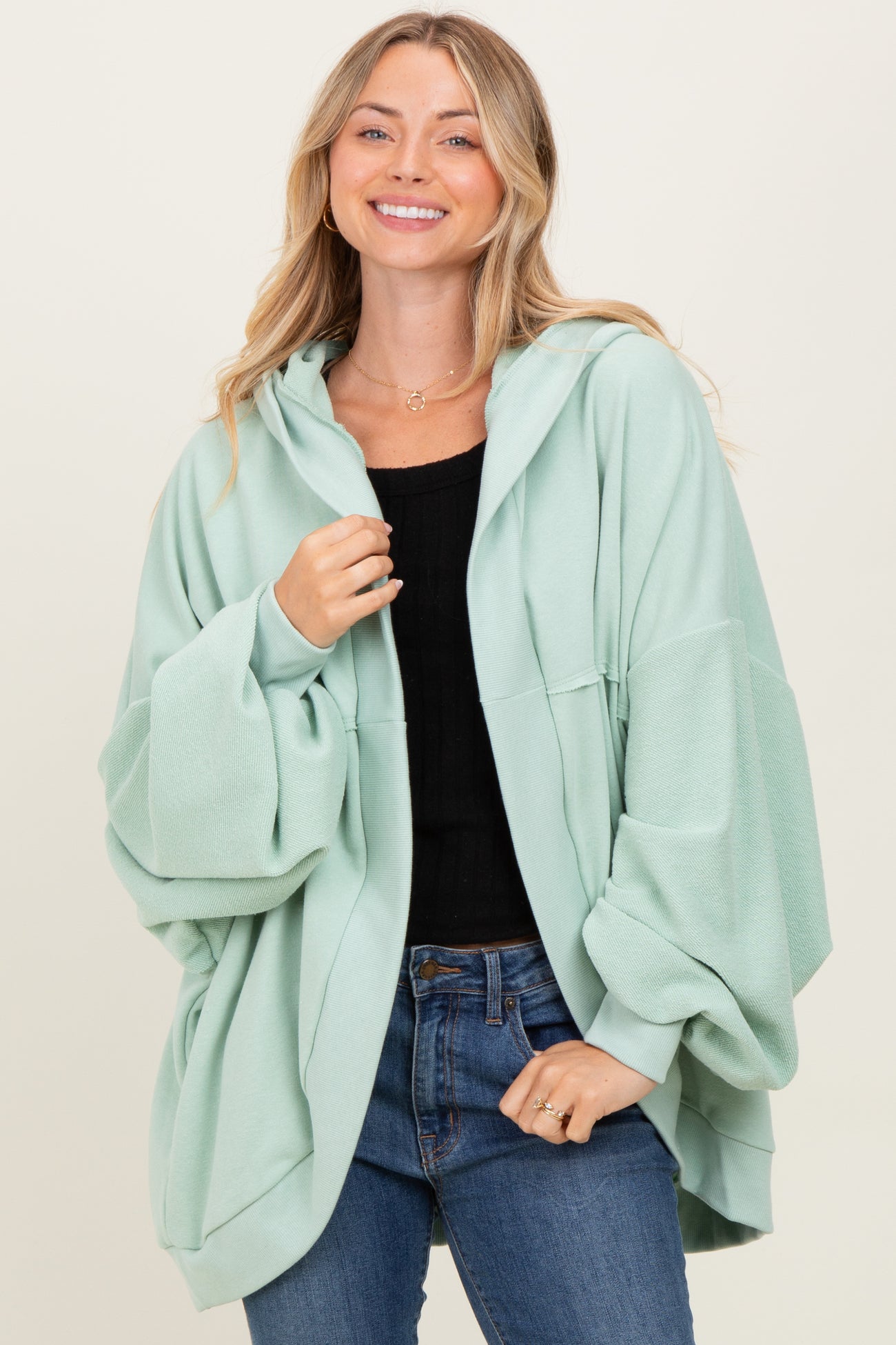 woman wearing a mint green oversized hoodie with wide sleeves and a front pocket, paired with blue jeans