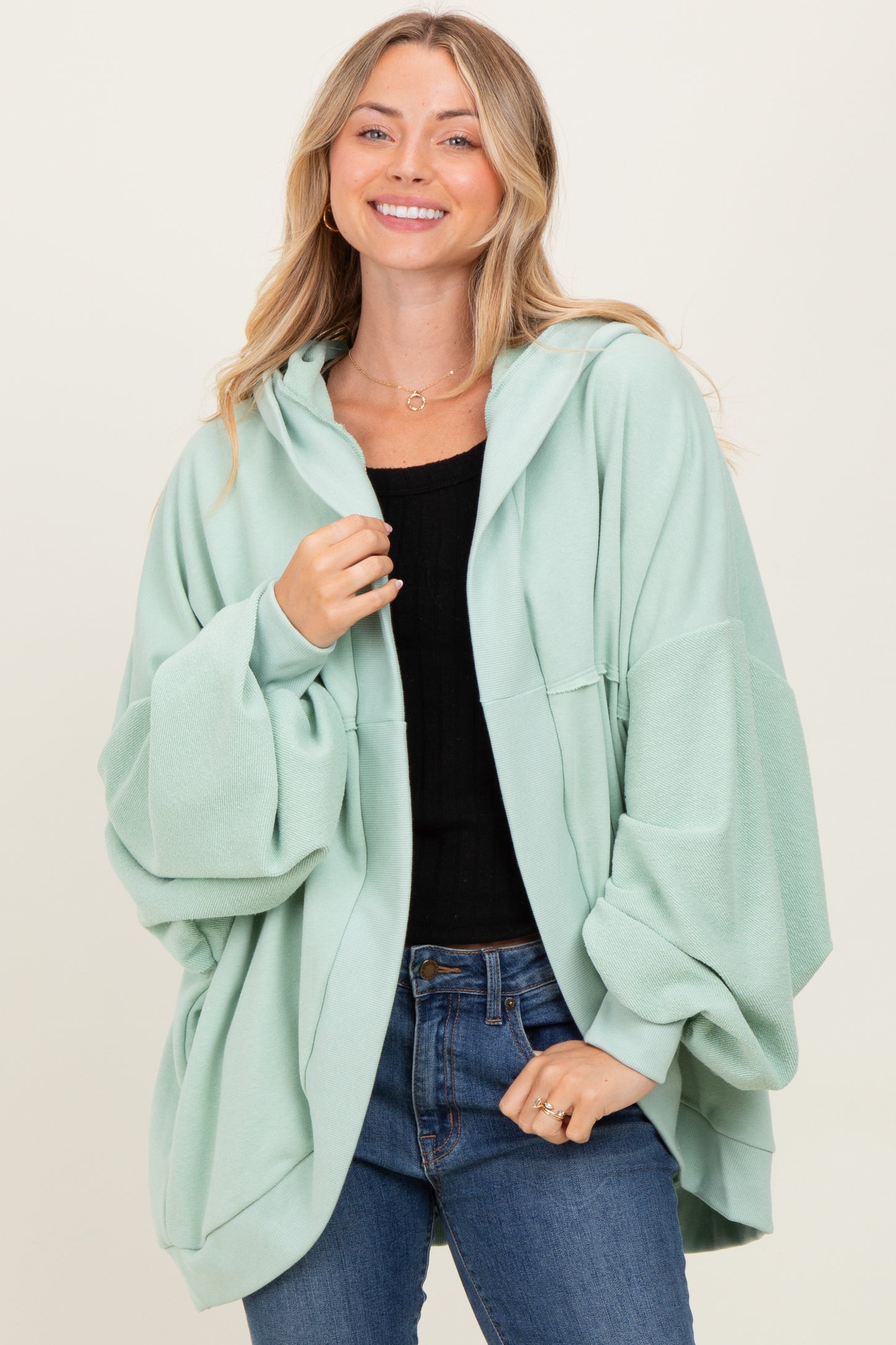 woman wearing a mint green oversized hoodie with wide sleeves and a front pocket, paired with blue jeans