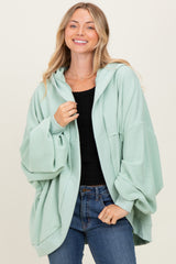 woman wearing a mint green oversized hoodie with wide sleeves and a front pocket, paired with blue jeans