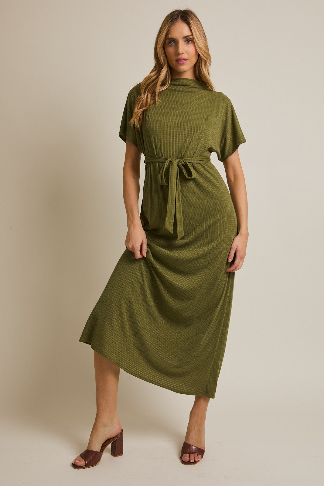 woman wearing a green midi dress with a tie belt and short sleeves, standing against a neutral background