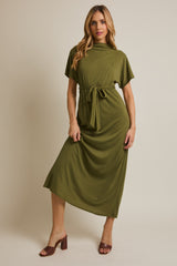 woman wearing a green midi dress with a tie belt and short sleeves, standing against a neutral background