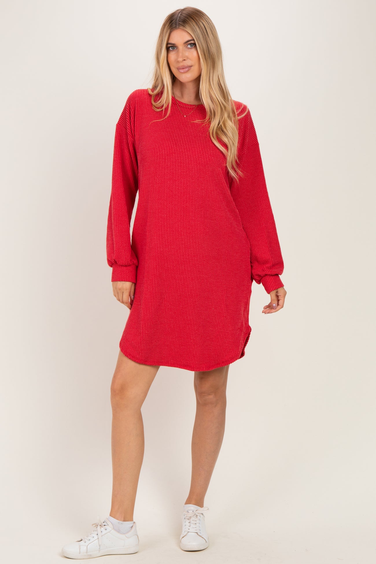 woman wearing a red ribbed long sleeve sweater dress with side slits and white sneakers