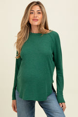 woman wearing a green long sleeve maternity top with a relaxed fit and side slits, showing her baby bump