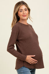 woman wearing a brown long sleeve maternity top with a rounded hem and holding her baby bump
