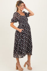 woman wearing a black floral print maternity dress with puffed sleeves and pockets, showcasing her baby bump