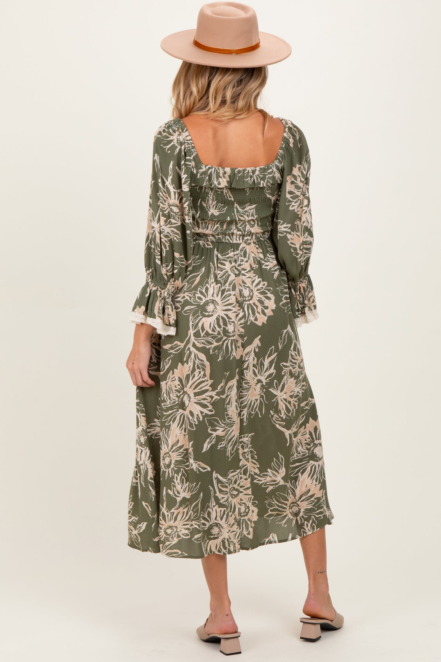 woman wearing a green floral print maternity dress with ruffled sleeves and a square back, styled with a hat