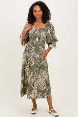 woman wearing an olive green floral maxi dress with puff sleeves and a tie detail, holding a handbag
