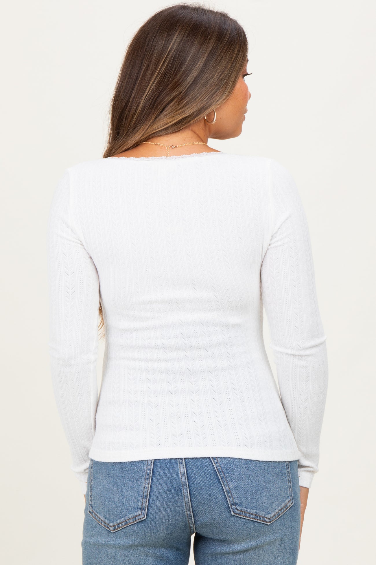 woman wearing a white long sleeve maternity top with a textured design and jeans, showing a fitted back view