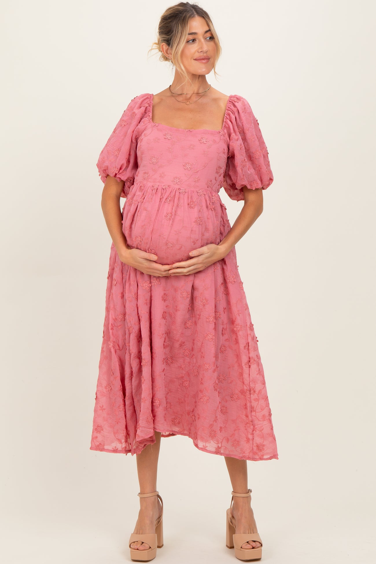 woman wearing a pink puff sleeve maternity dress with floral details and holding her baby bump