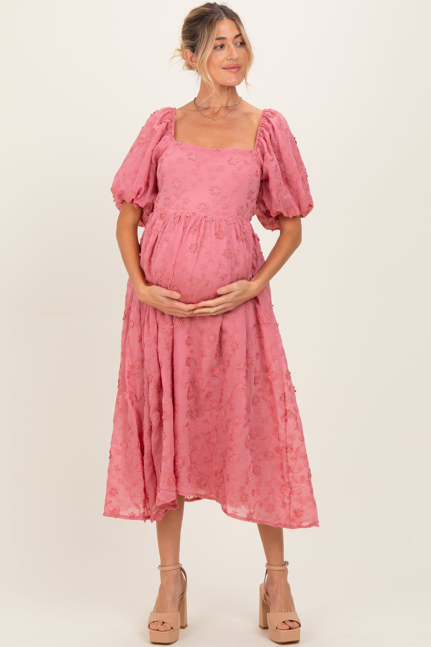 woman wearing a pink puff sleeve maternity dress with floral details and holding her baby bump