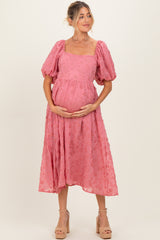 woman wearing a pink puff sleeve maternity dress with floral details and holding her baby bump