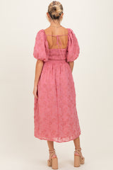 woman wearing a pink floral embroidered maternity dress with puff sleeves and a smocked back, showing her baby bump