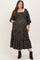 woman wearing a black floral maternity plus dress with a square neckline and puff sleeves, featuring a tiered skirt and pockets