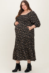 woman wearing a black floral maternity dress with a square neckline and pockets, showing her baby bump