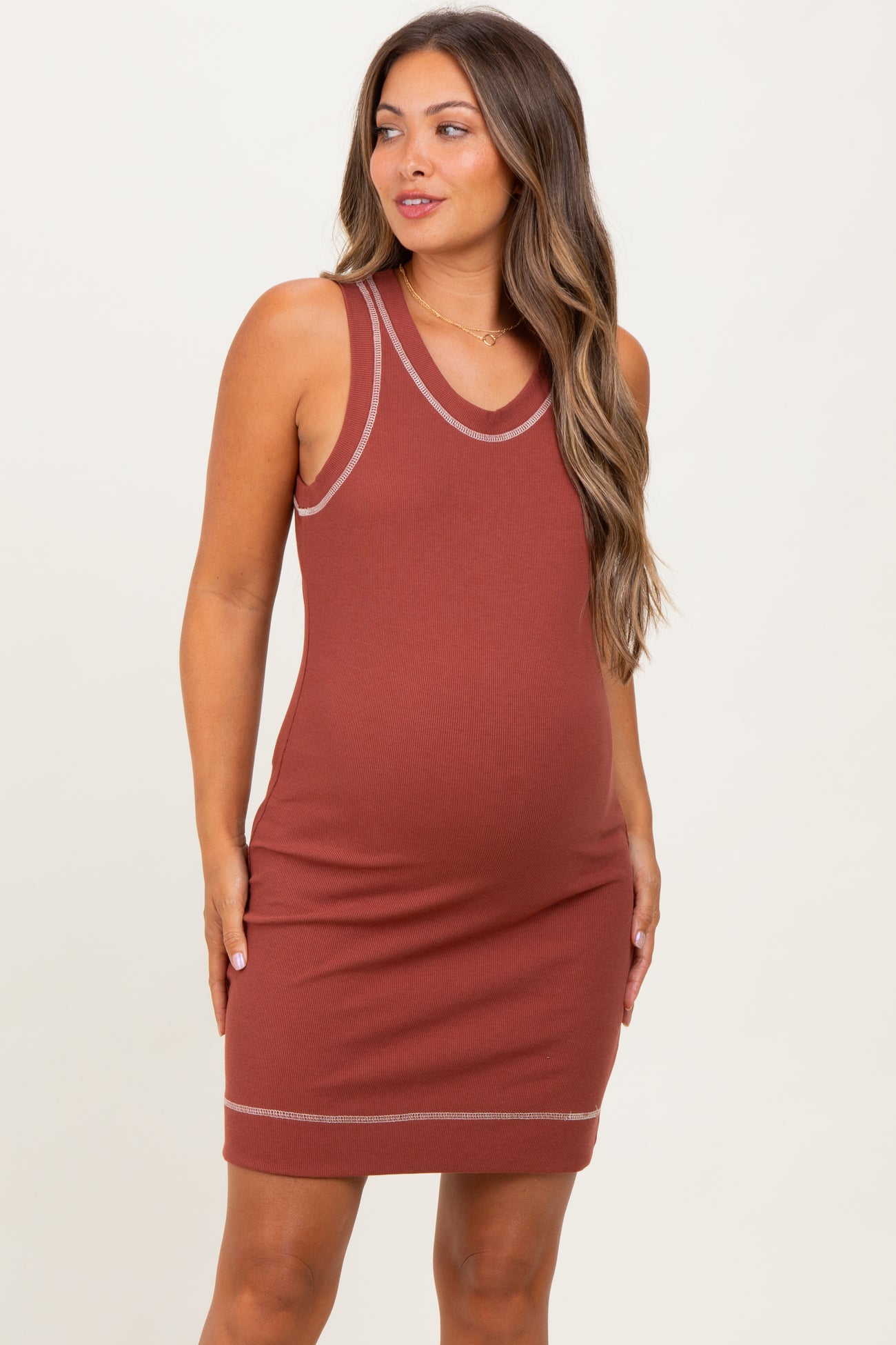 woman wearing a rust-colored maternity tank dress with ribbed texture and contrasting trim, showcasing her baby bump