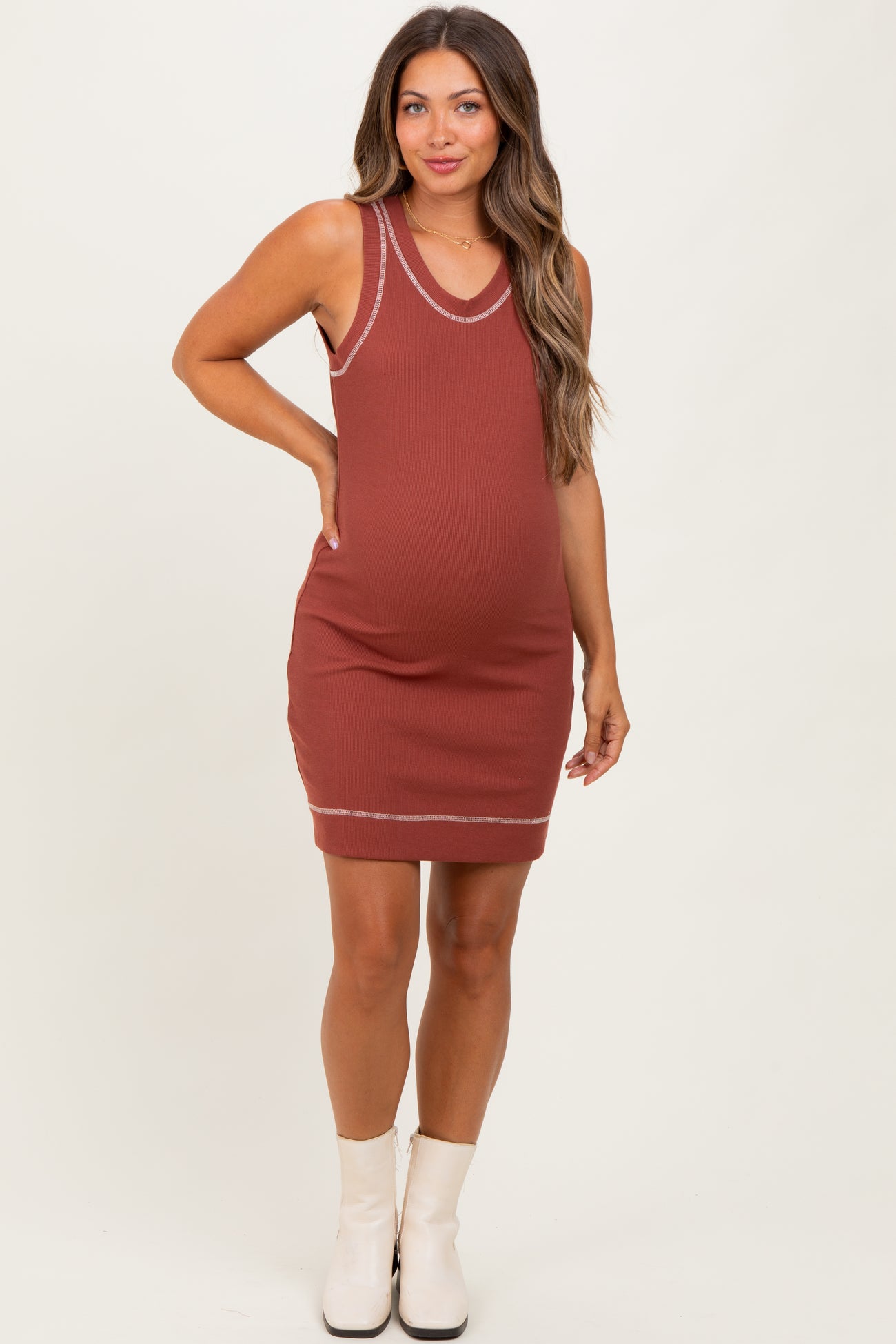 woman wearing a rust colored sleeveless maternity dress with white trim and a visible baby bump