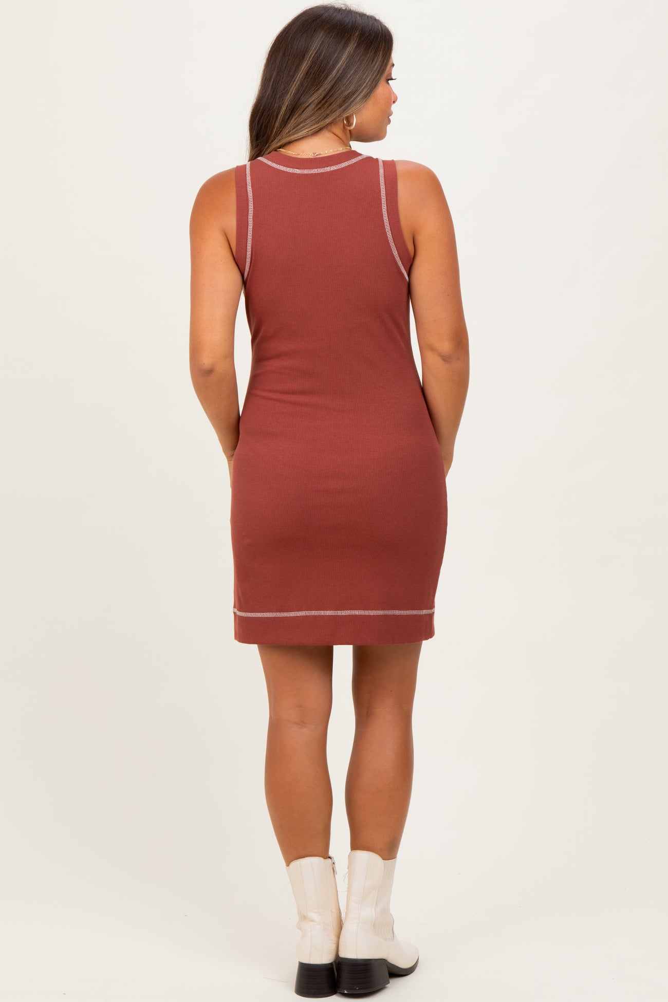 woman wearing a rust colored sleeveless maternity dress with contrast stitching and a fitted silhouette