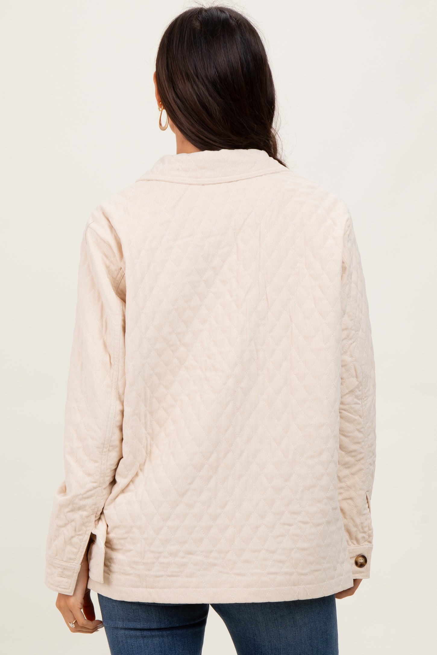 woman wearing a beige quilted jacket, view from the back, with flap collar and button detail on sleeves