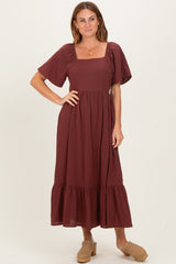 woman wearing a burgundy maxi dress with a square neckline and puff sleeves, styled with tan clogs