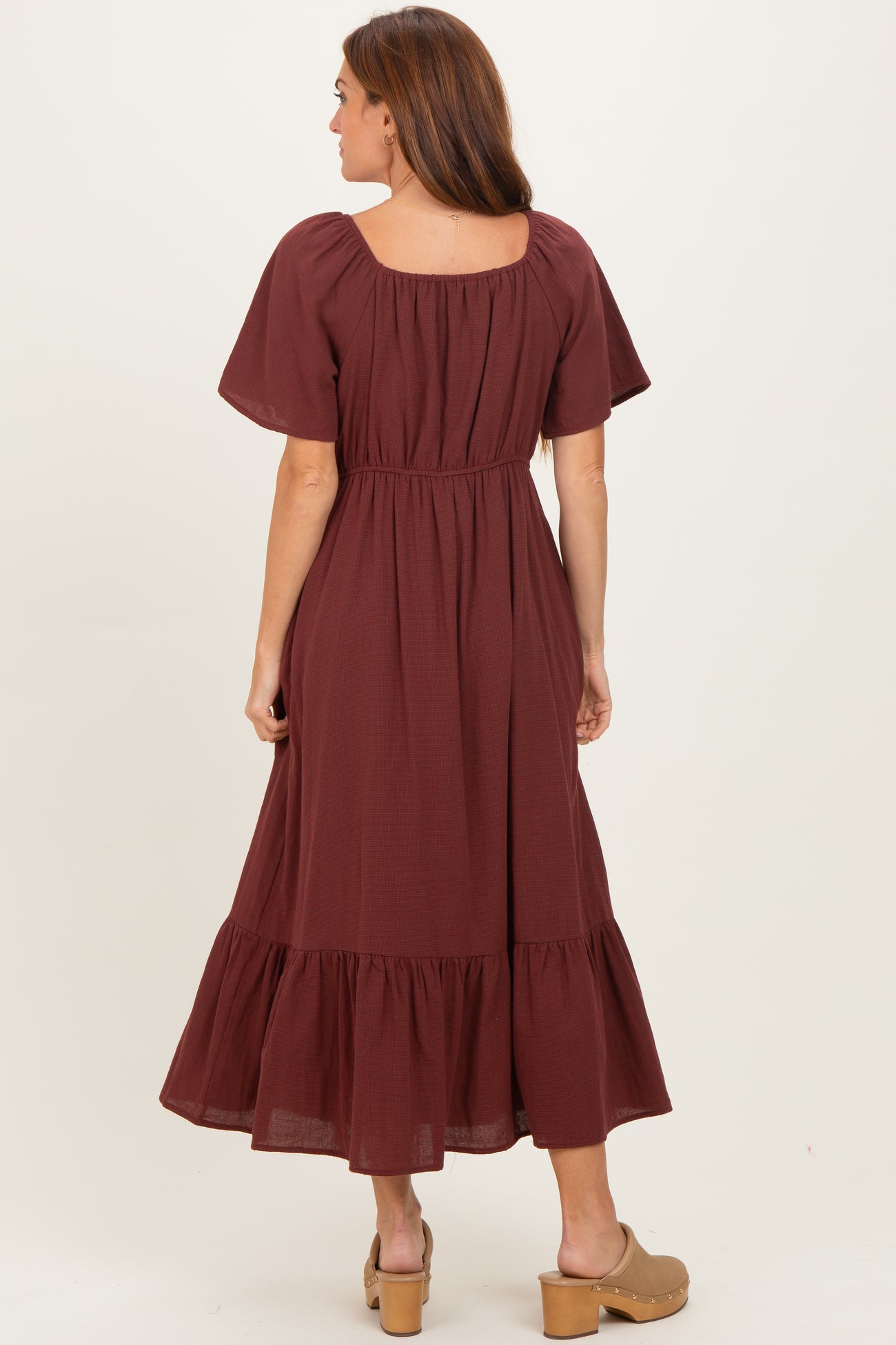 woman wearing a burgundy short sleeve maxi dress with a gathered waist and tiered hem, viewed from the back