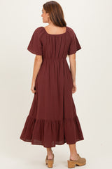 woman wearing a burgundy short sleeve maxi dress with a gathered waist and tiered hem, viewed from the back