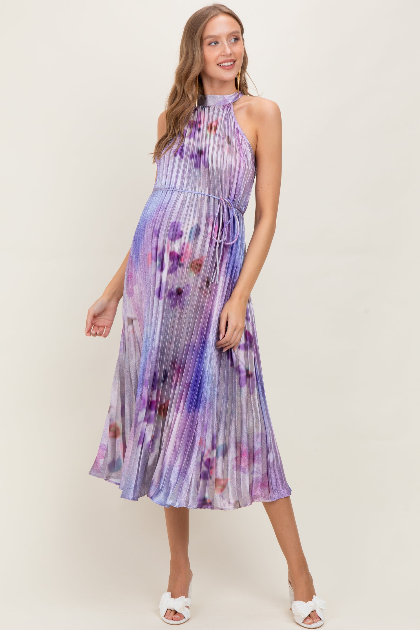 woman wearing a purple floral pleated maternity dress with a waist tie and a visible baby bump