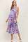 woman wearing a purple floral pleated maternity dress with a waist tie and a visible baby bump