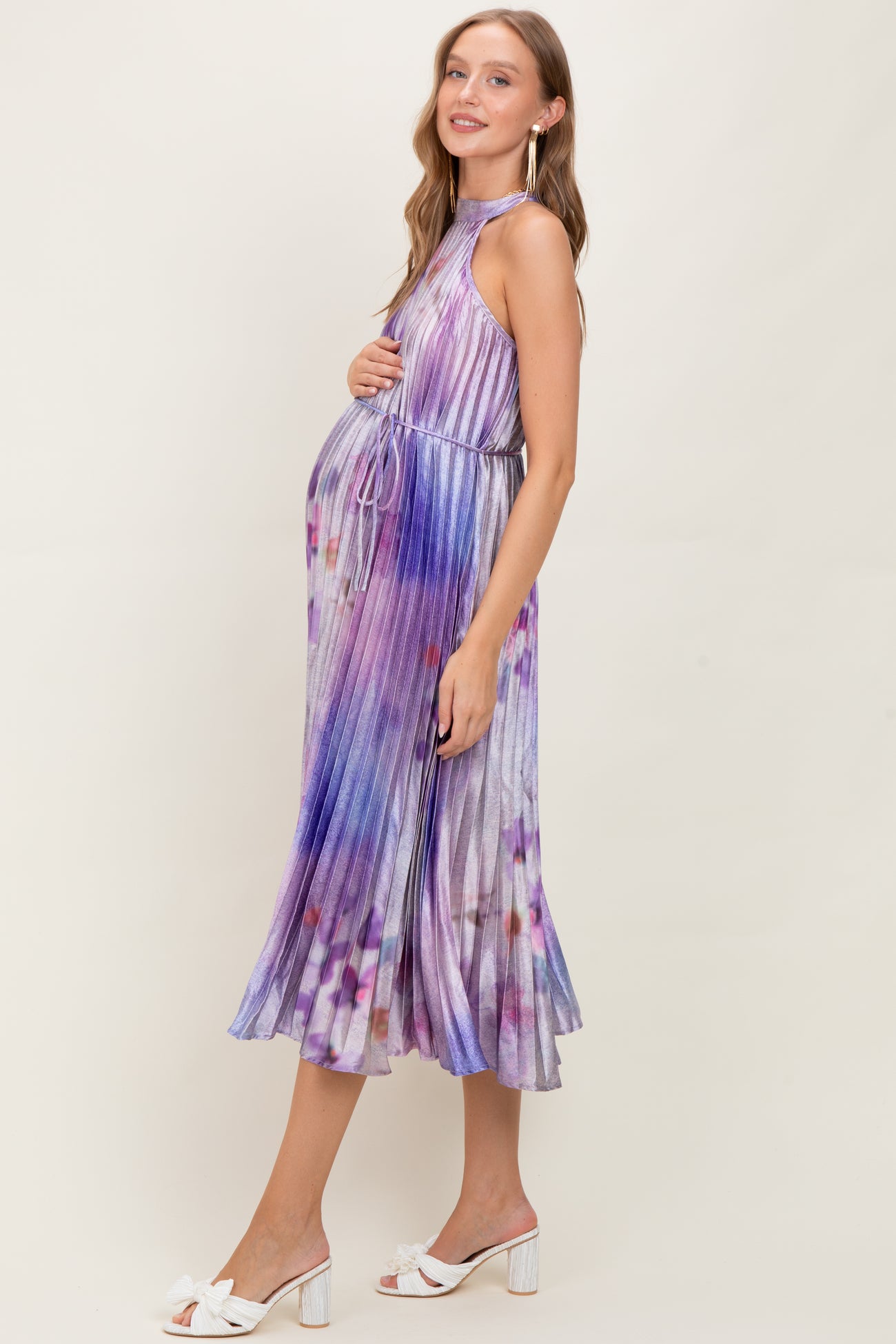 woman wearing a purple tie-dye halter neck maternity dress with a baby bump, styled with white sandals