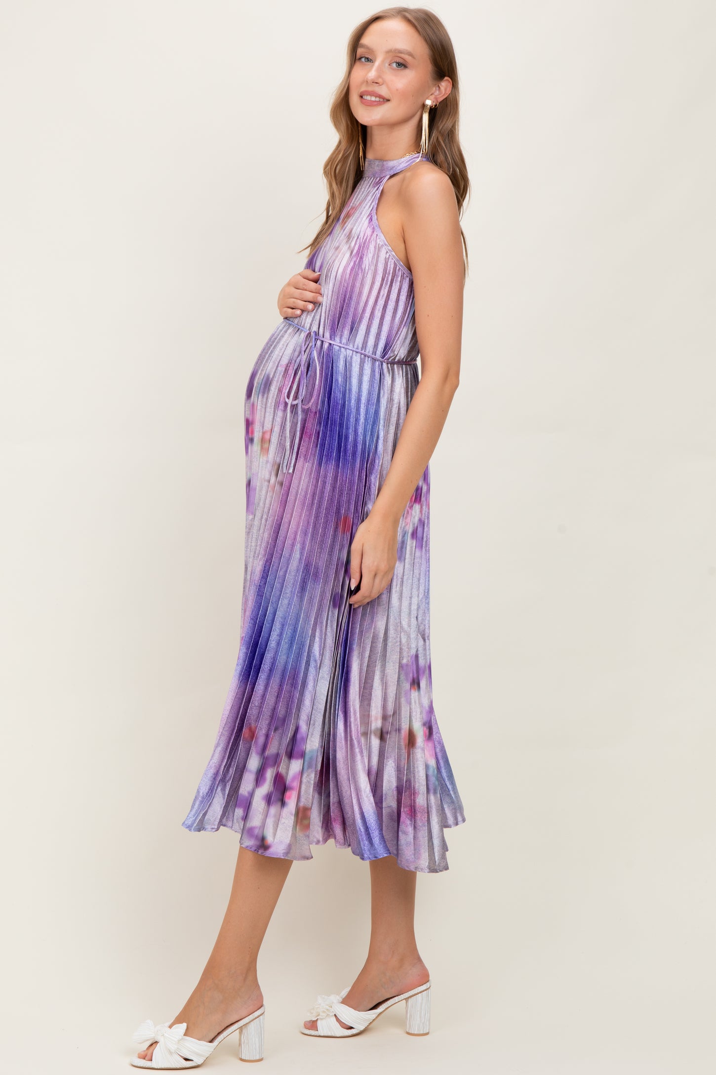 woman wearing a purple tie-dye halter neck maternity dress with a baby bump, styled with white sandals