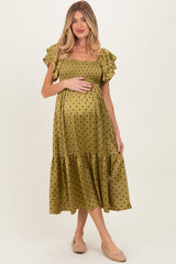 woman in an olive green dotted maternity dress with ruffled sleeves, gently holding her baby bump