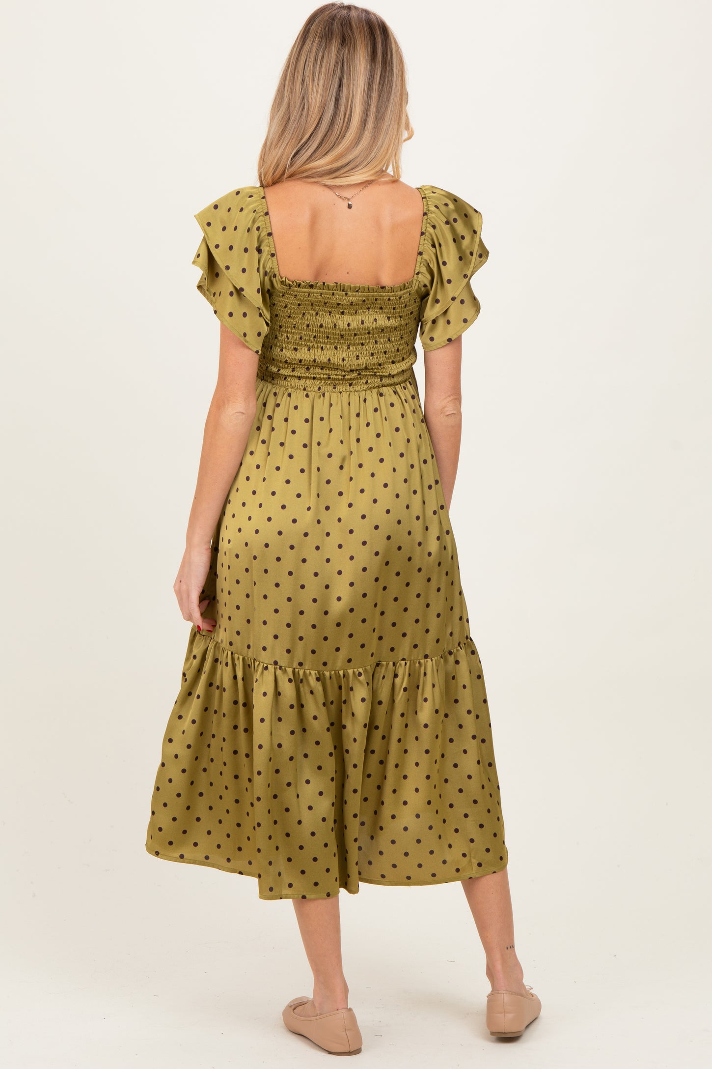 woman wearing a green polka dot maternity dress with ruffled sleeves and a smocked bodice, showing her back