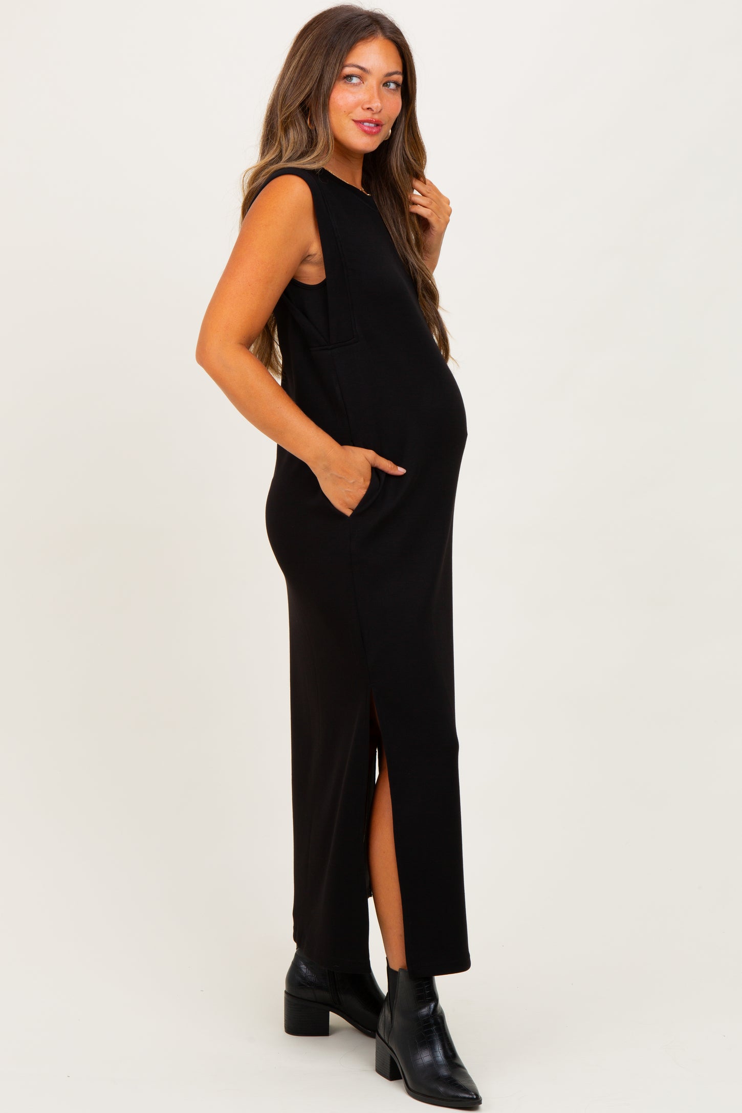 woman wearing a black sleeveless maternity dress with side pockets and a side slit, showcasing her baby bump